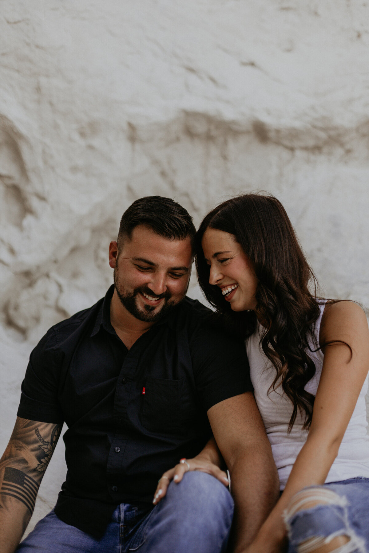 engaged couple sitting on a white rock together laughing