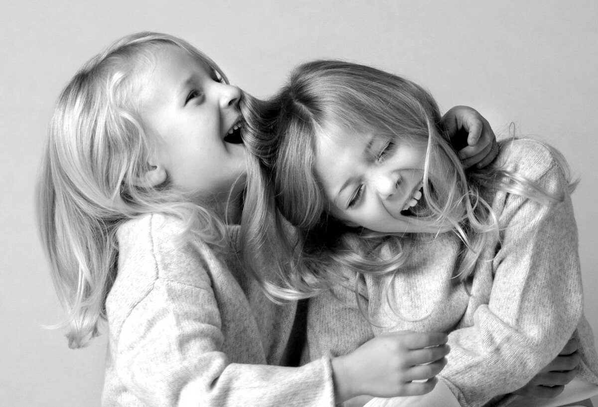 Two young children with long hair, laughing joyfully while hugging. The black-and-white image conveys happiness and warmth, creating a playful and affectionate mood.