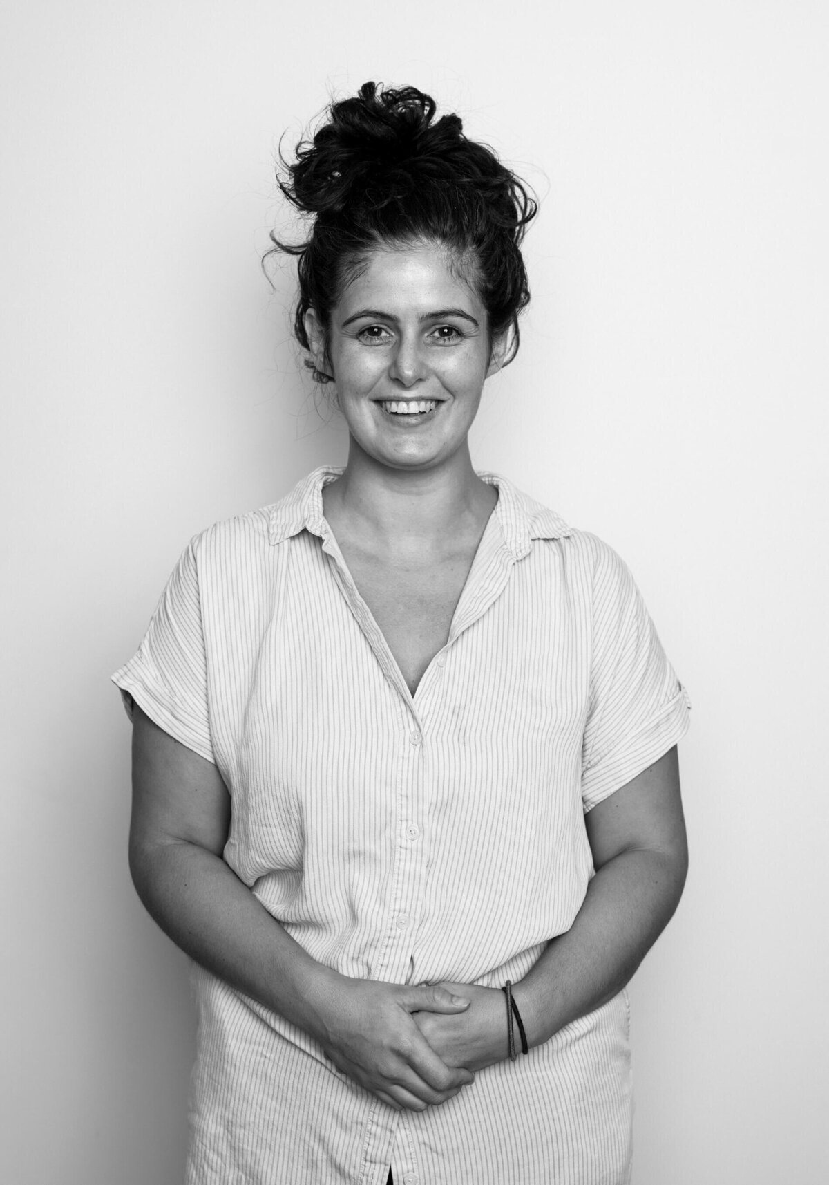 Studio before shot of a woman in a casual dress, smiling with her hair in a bun.