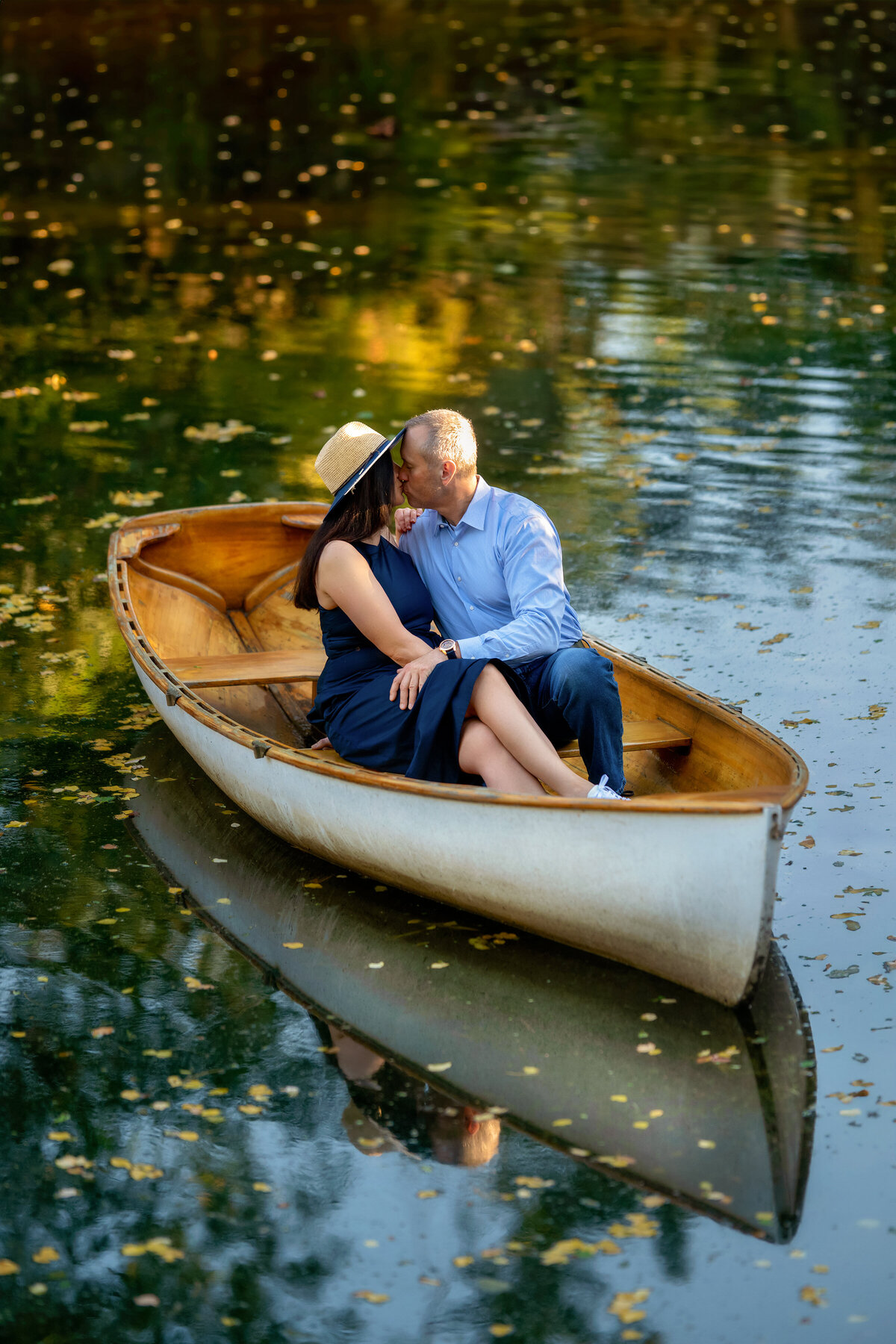 wooden boat reflecting on the lake as  engaged couple kissing in it