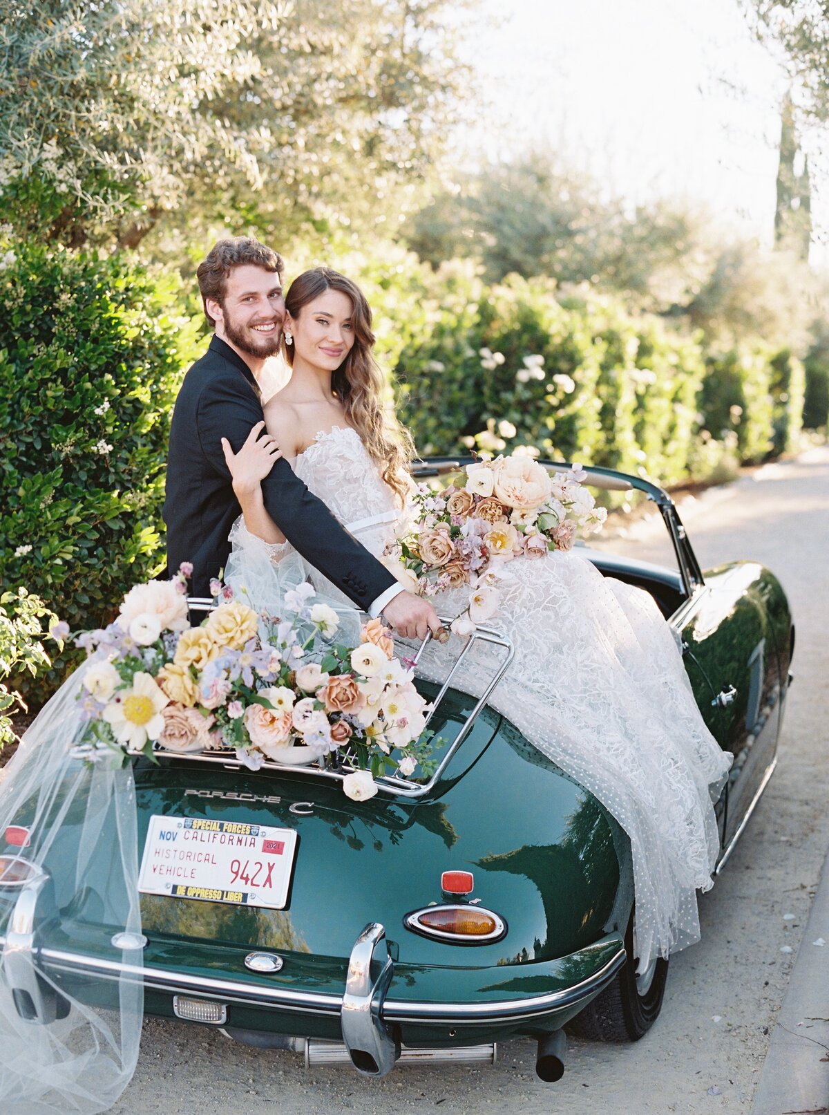 bride and groom sitting on a vintage dark green car with flowers
