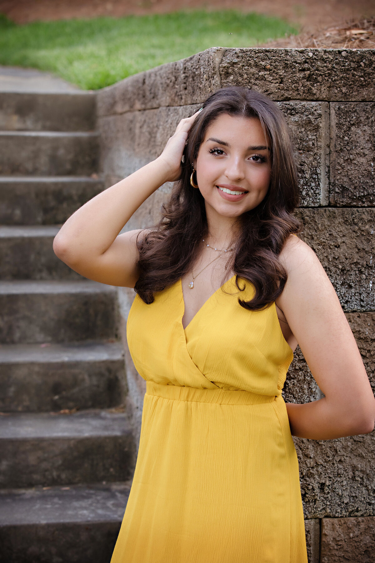 Senior portrait in yellow dress standing in front of a concrete staircase, blending formal style with urban textures.