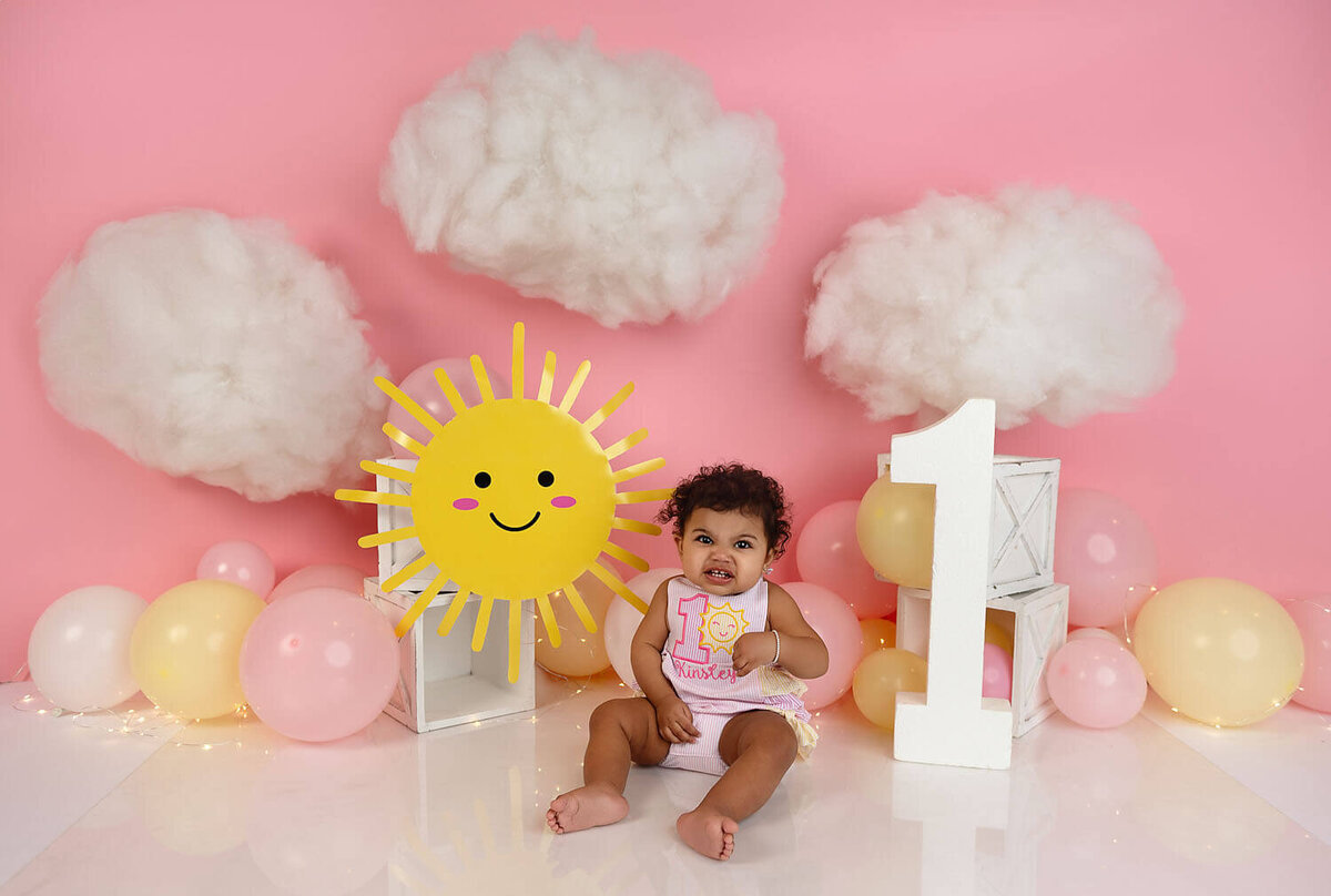 A young toddler sits in a studio set celebrating her first birthday