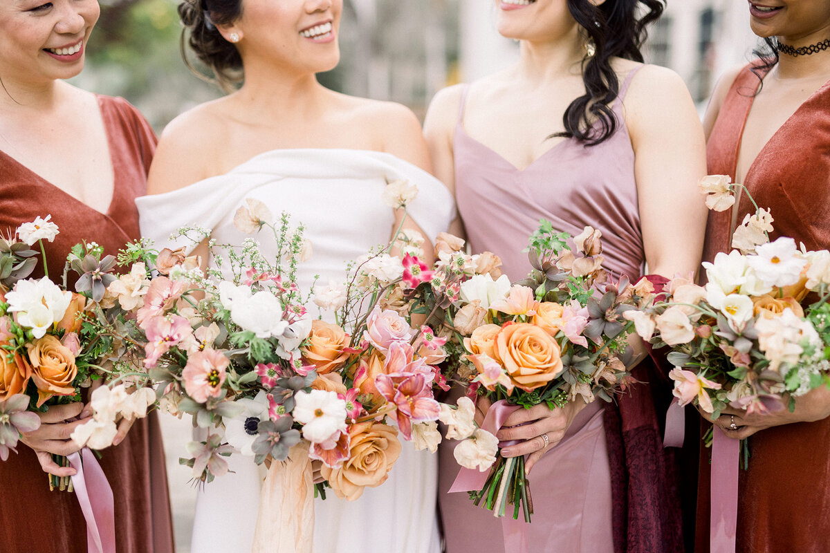 bride and bridesmaids holding bouquets of spring flowers mauve burnt orange and dusty rose