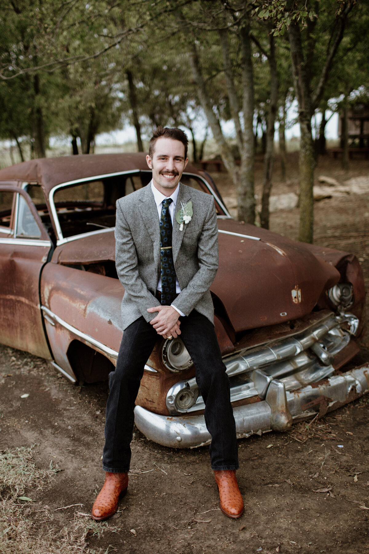 A groom sits on an old classic car at Chapel Creek Ranch in Denton Texas. Captured by Fort Worth Wedding Photographer, Megan Christine Studio