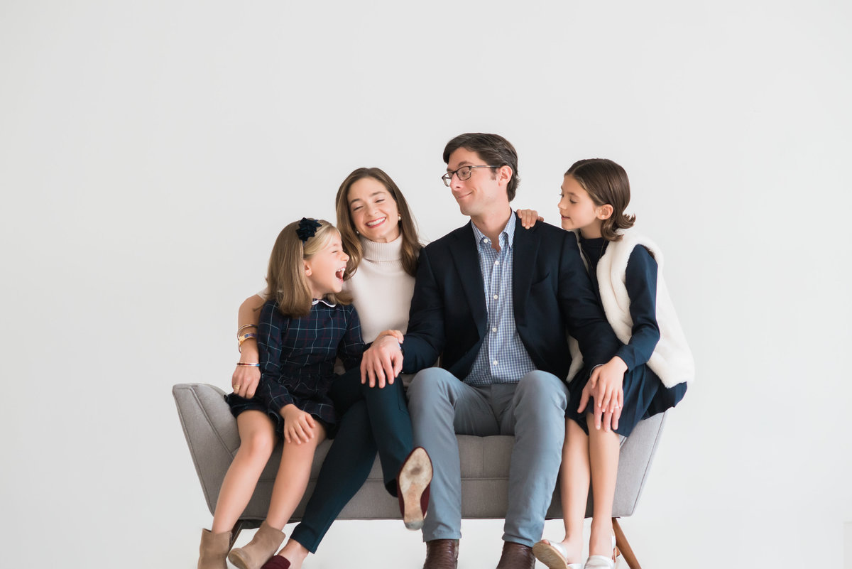 daughters in navy dresses sitting with parents in white portrait studio on grey modern bench