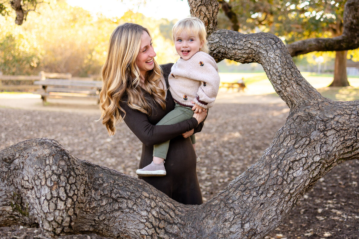 Mother holding her smiling toddler on a tree branch at Laurelwood Park San Mateo featured in the Bay Area Family Portfolio, Ellobelle Photography