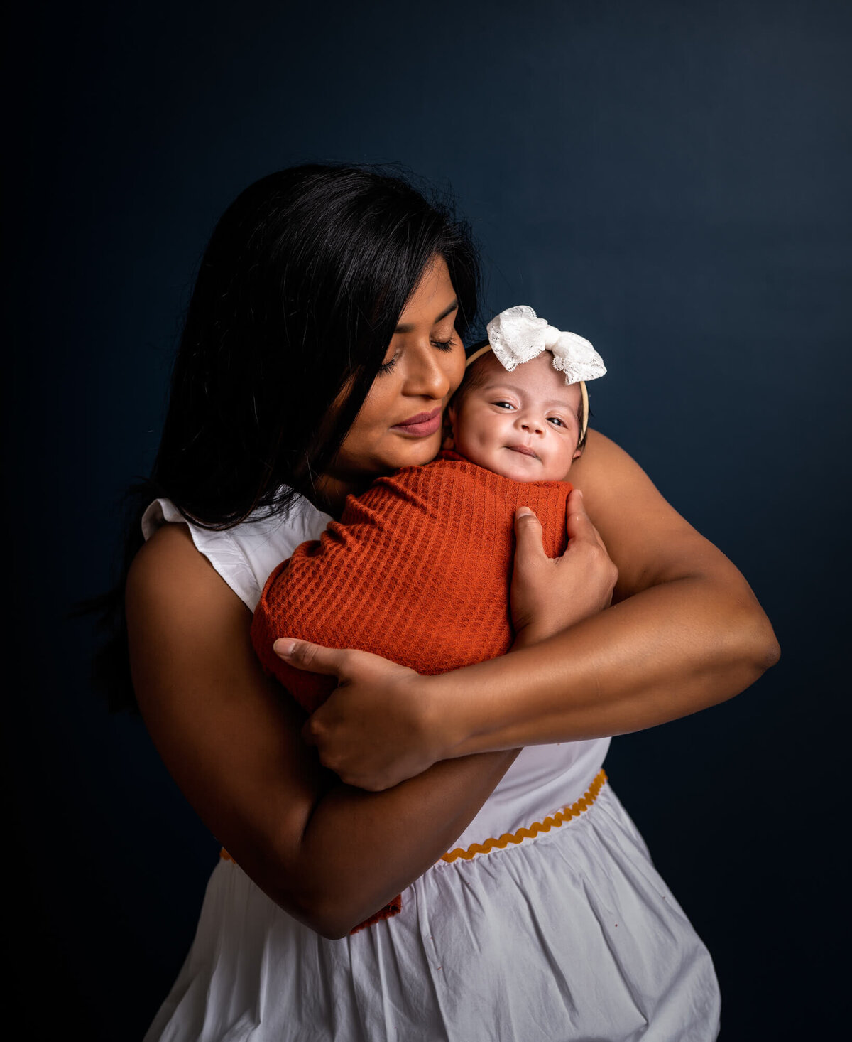 A new mama cuddles her newborn baby daughter who is wrapped in an orange blanket r