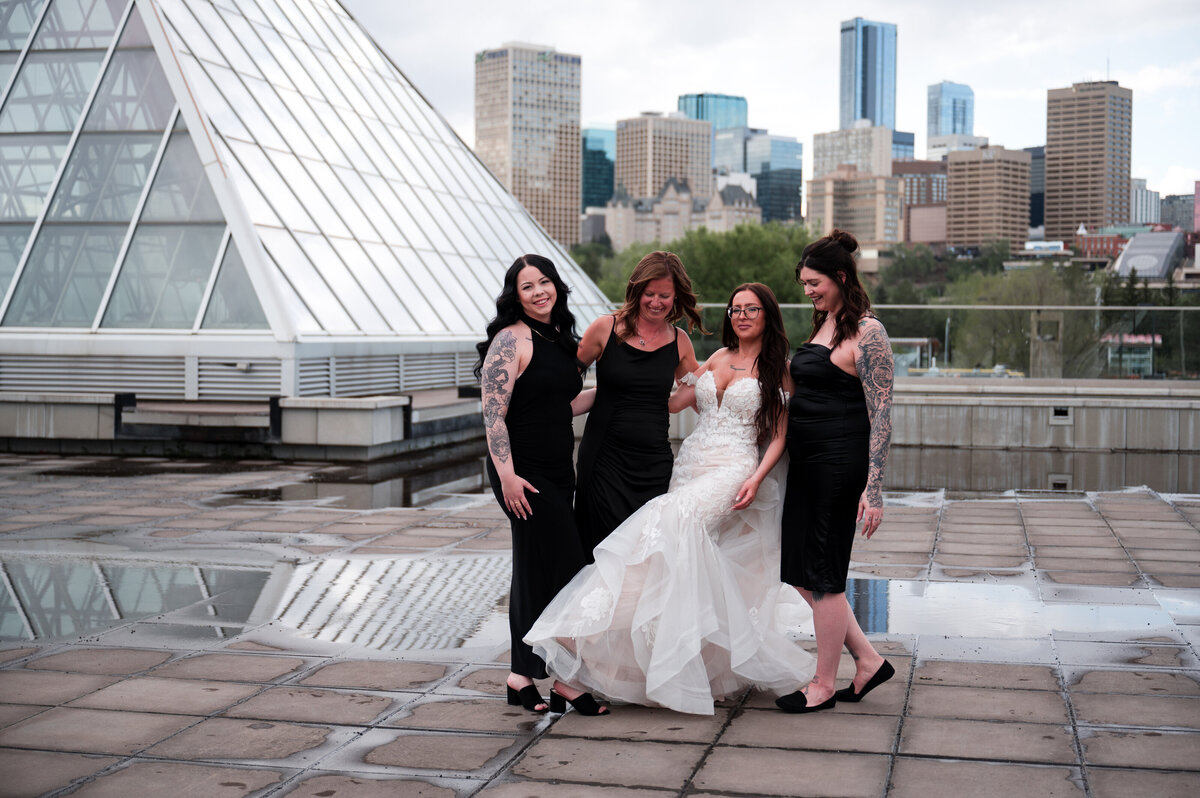 bride and her bridesmaids smiling and laughing for a wedding portrait outside of the Muttart Conservatory in Edmonton, Alberta