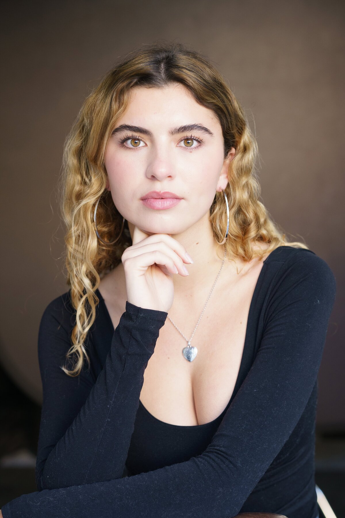 Young woman with a low-cut dark dress posing in a sultry manner for a modeling headshot