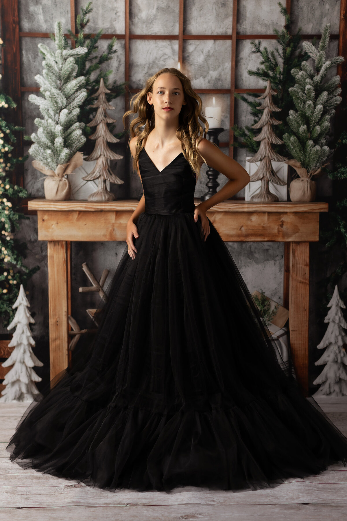 Dallas senior photographer captures a young woman in a black gown against a winter-themed backdrop with snowy trees and a rustic wooden setup. The shoot combines festive elegance and senior photography, showcasing a luxurious yet serene moment in a high-fashion style. Perfect for those seeking timeless senior photos in Dallas.