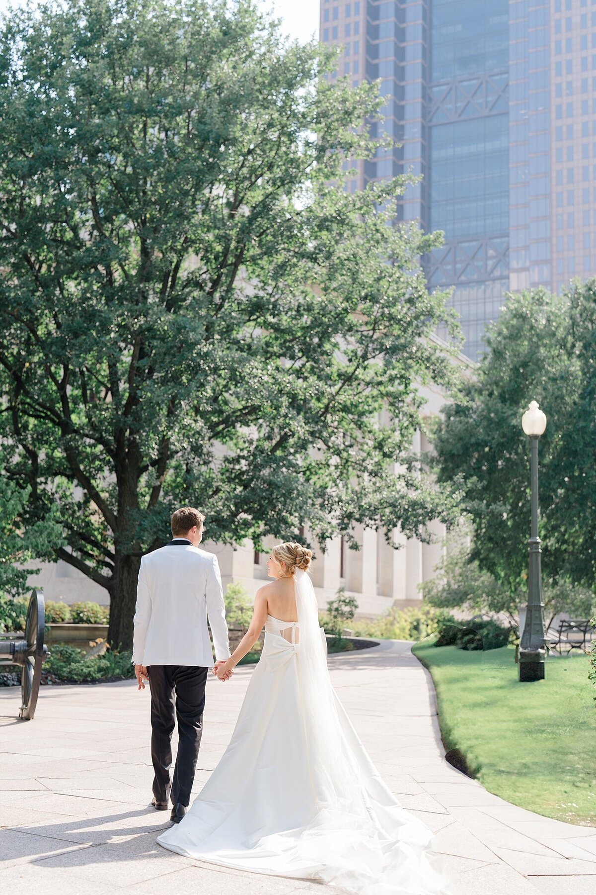 Columbus wedding  photographer photographs bride and groom holding hands and the bride smiling up at her groom as they walk through a park in Columbus