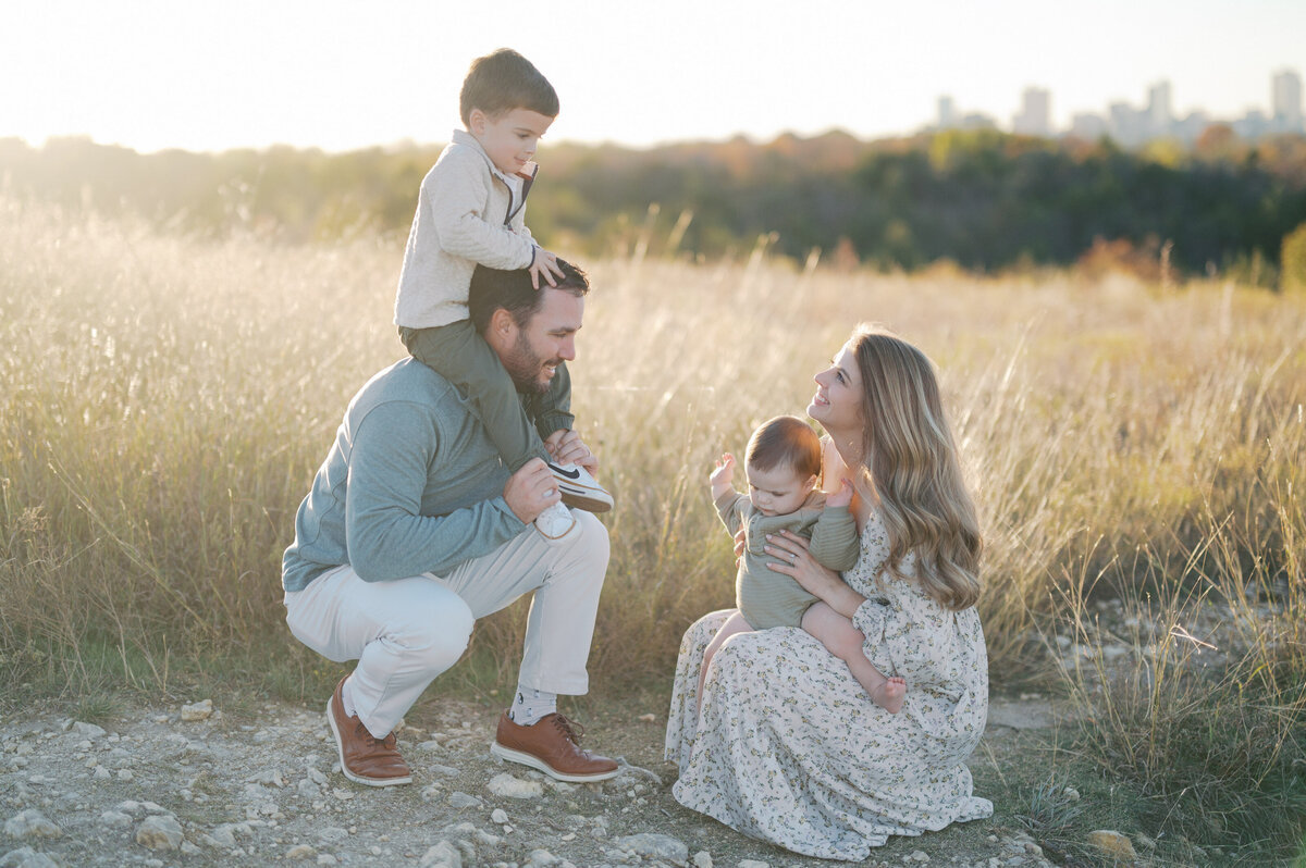 family kneels down in tall grass smiling at each other during fort worth family photos