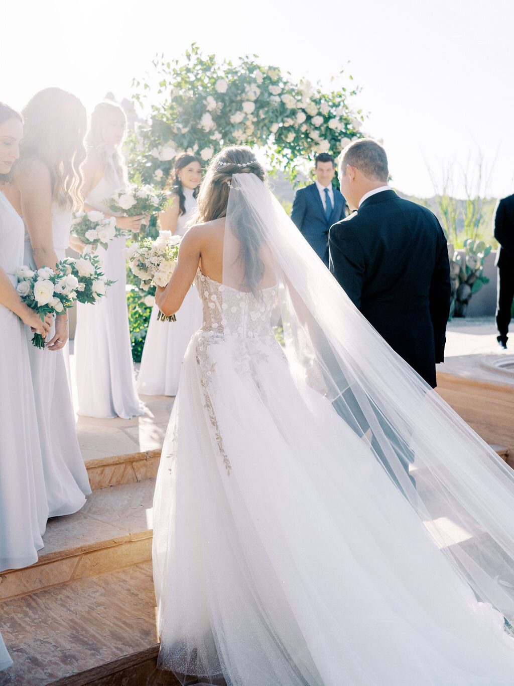 A touching wedding moment as the bride walks down the aisle with her father, surrounded by bridesmaids in matching dresses. A timeless wedding tradition captured beautifully.