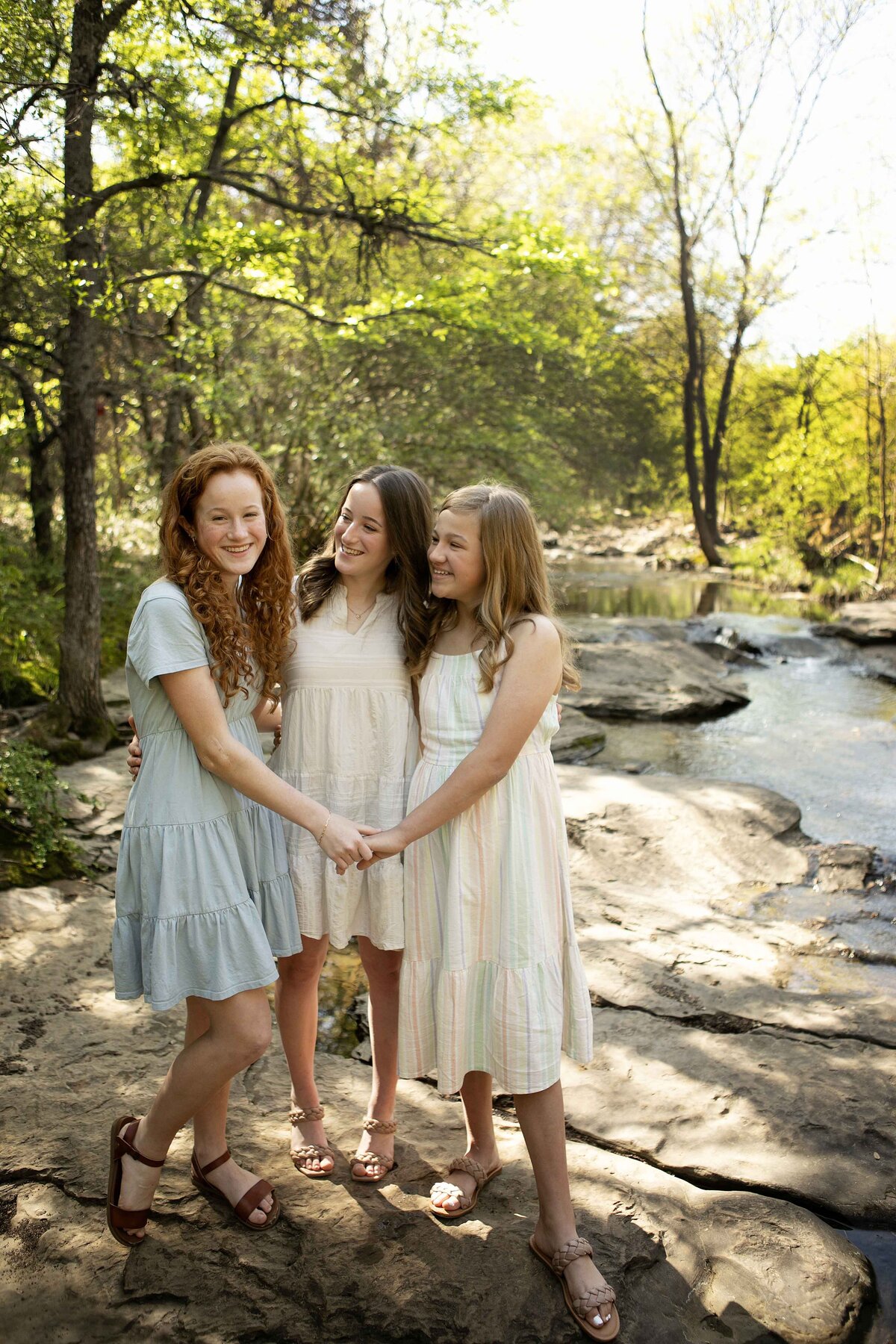 Sisters standing close together near the creek in Flower Mound, their smiles lighting up the natural backdrop during their photoshoot