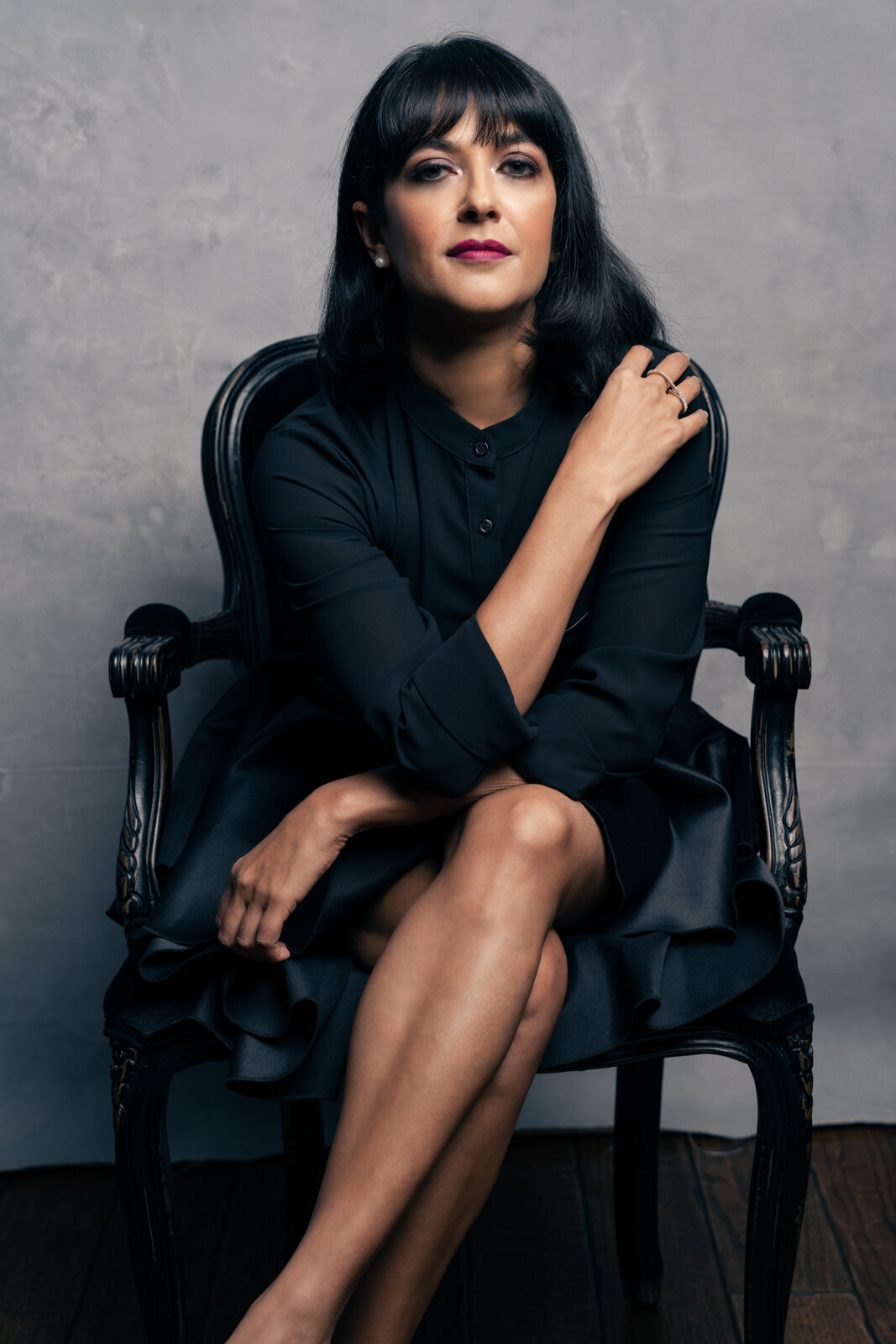 Picture on a young woman with dark hair, sitting on a chair in a black dress