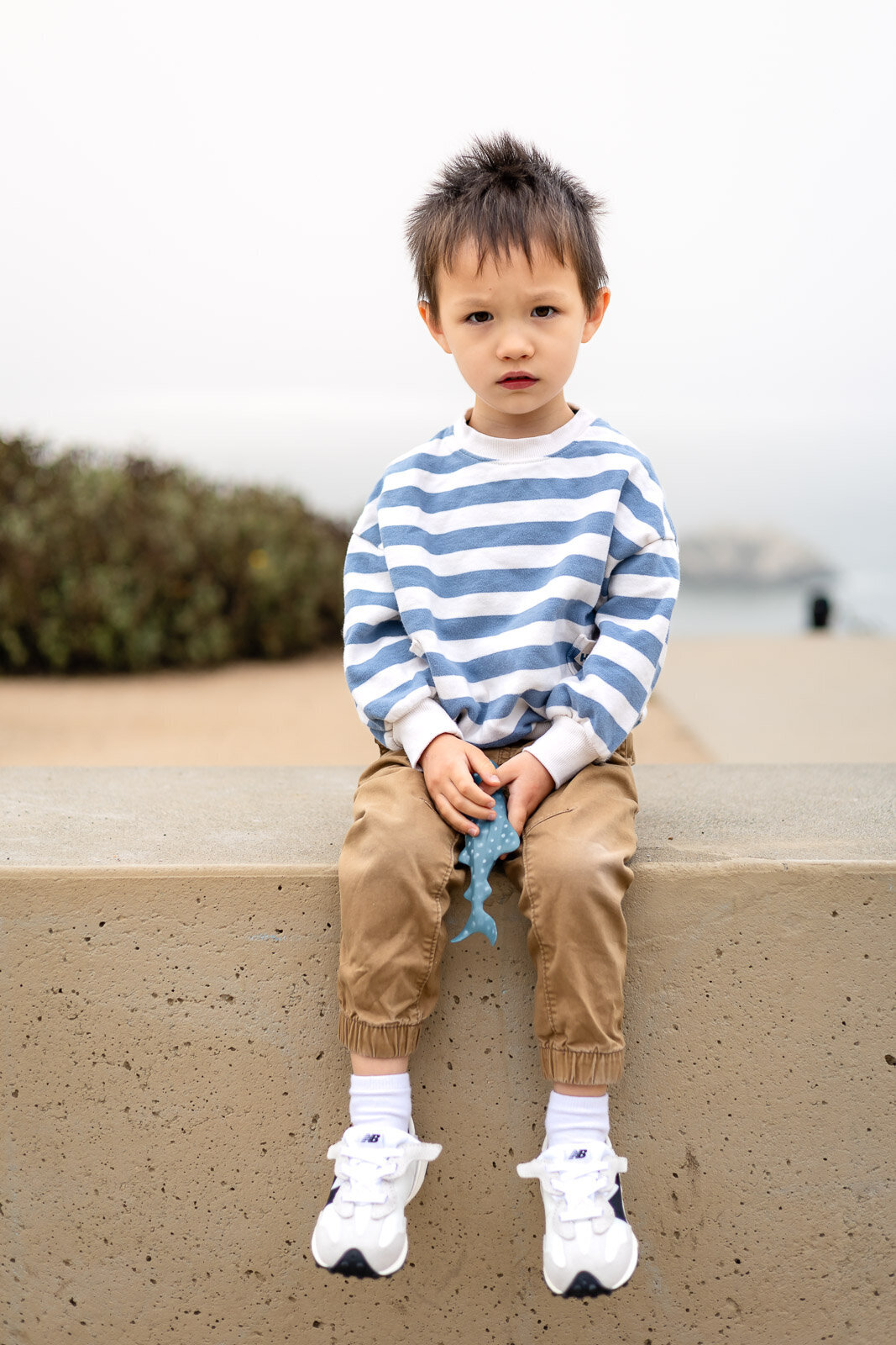 Young boy sitting on a concrete wall at the beach during Bay Area School Photography Lifestyle session – Ellobelle Photography