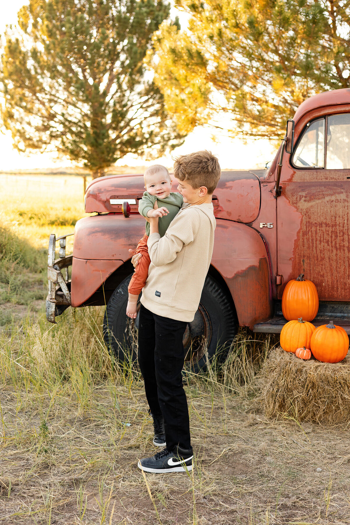 Preteen boy holds baby brother and looks at him while baby looks at the camera.