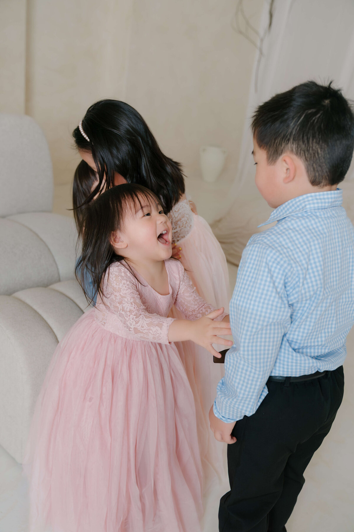 Little girl in a pink dress playfully reaching for her older brother during a family session.