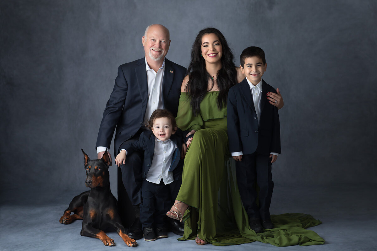A family poses together, dressed in formal attire, with their Doberman dog, captured by a Dallas family photographer.