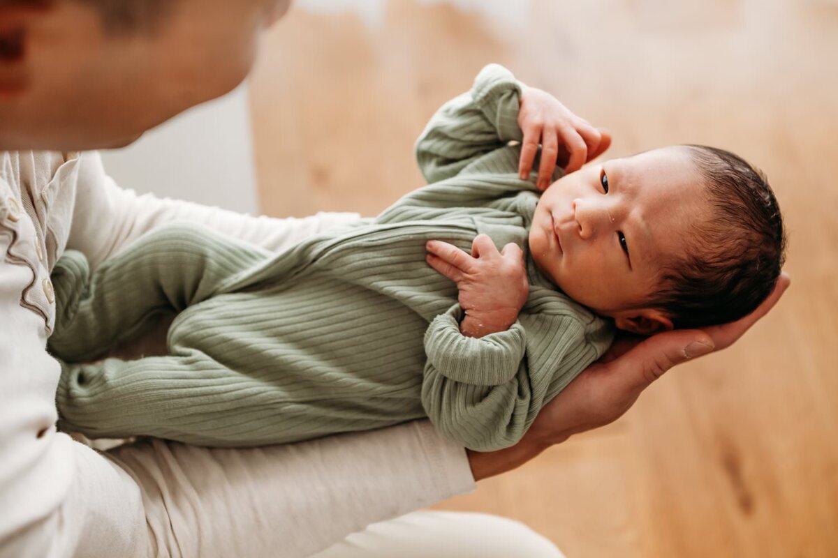 baby in dads arms appears to be looking up at dad through sleepy eyes.