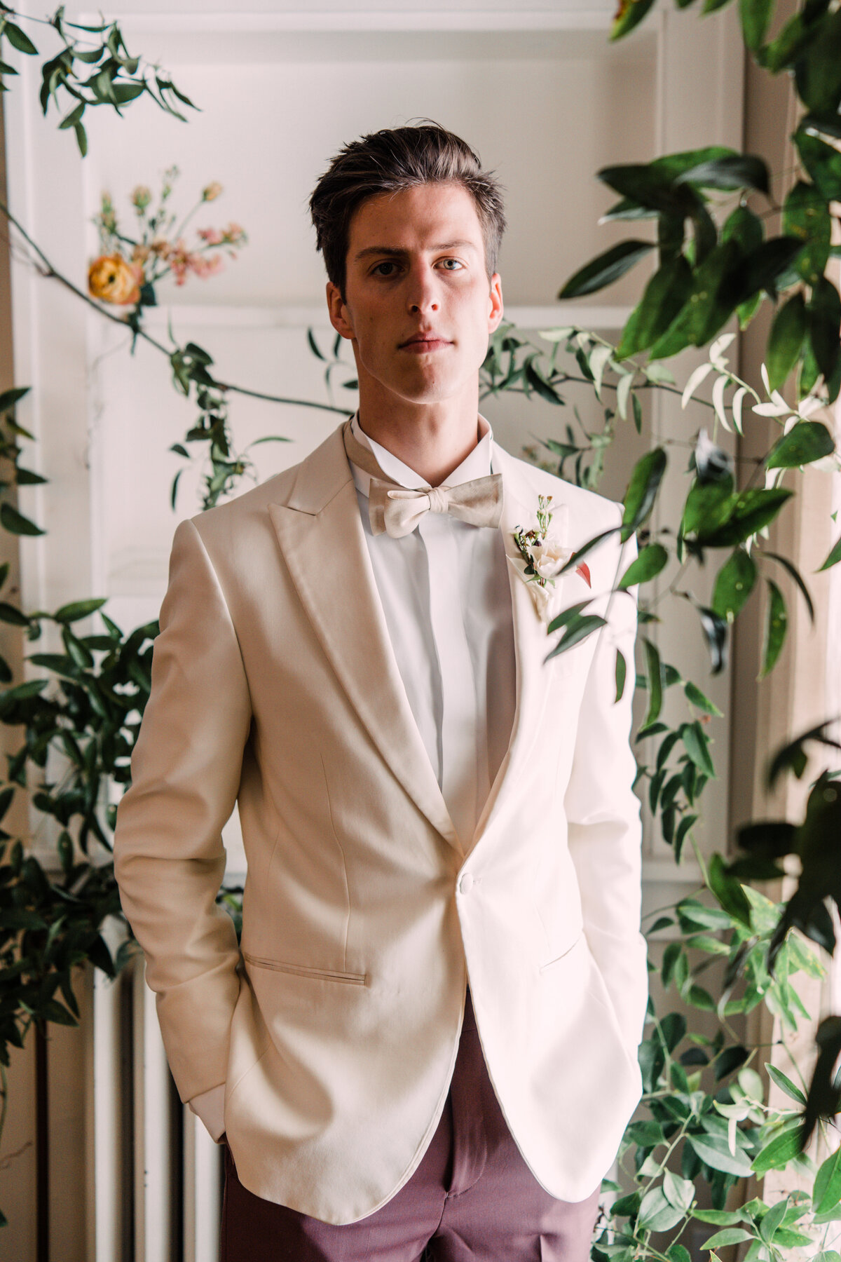 Headshot of groom wearing white tuxedo jacket & bow tie surrounded by vines