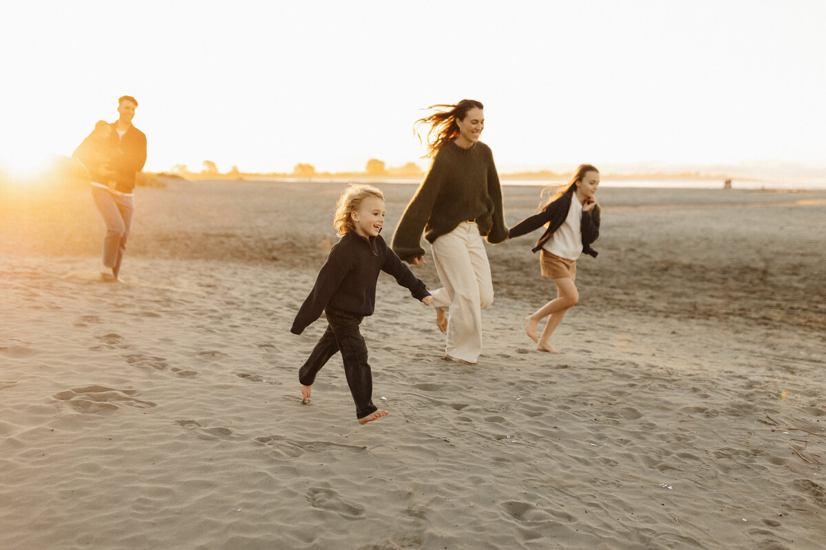a mother and her two children running along the beach at sunset during a christchurch family photoshoot with professional photographer lucy jane