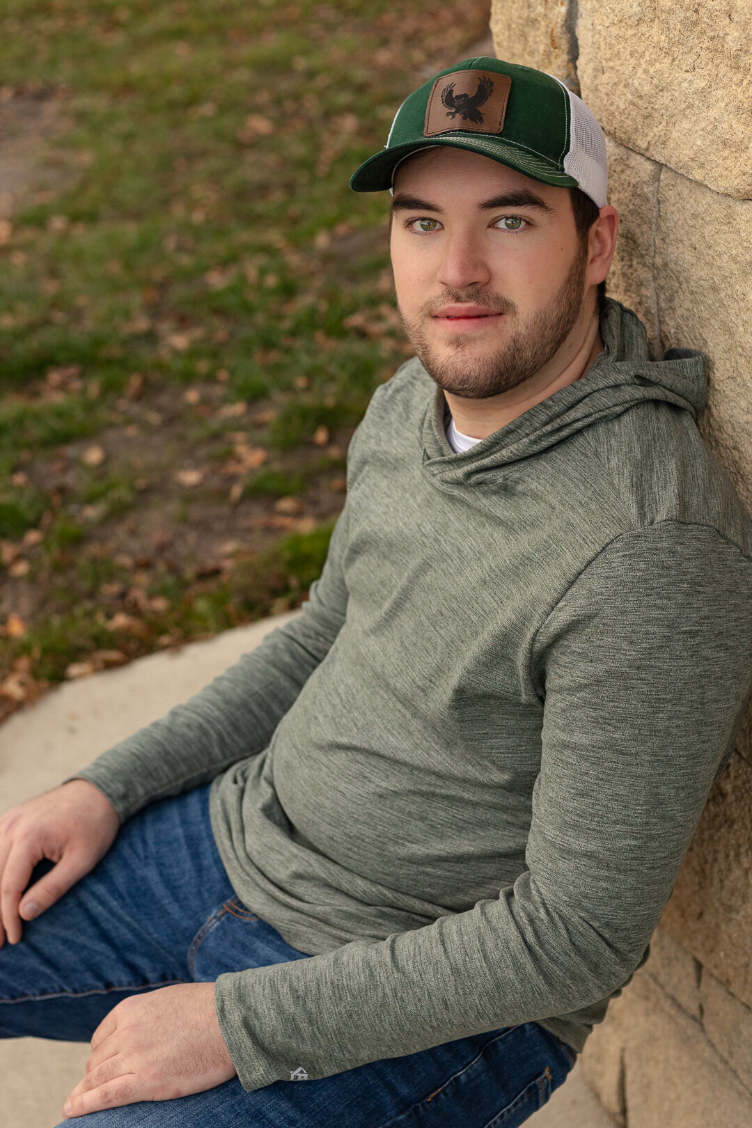 A senior guy sitting leaning against a brick wall in Lawrence KS
