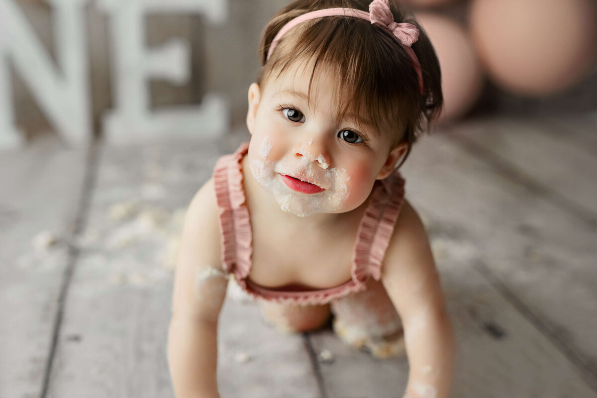 baby girl crawling with a pink outfit and cake on her face during a one year old session