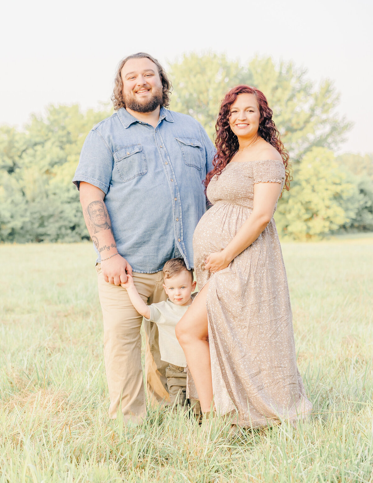 mom, dad, and son holding hands while posing in field during maternity photo shoot in field