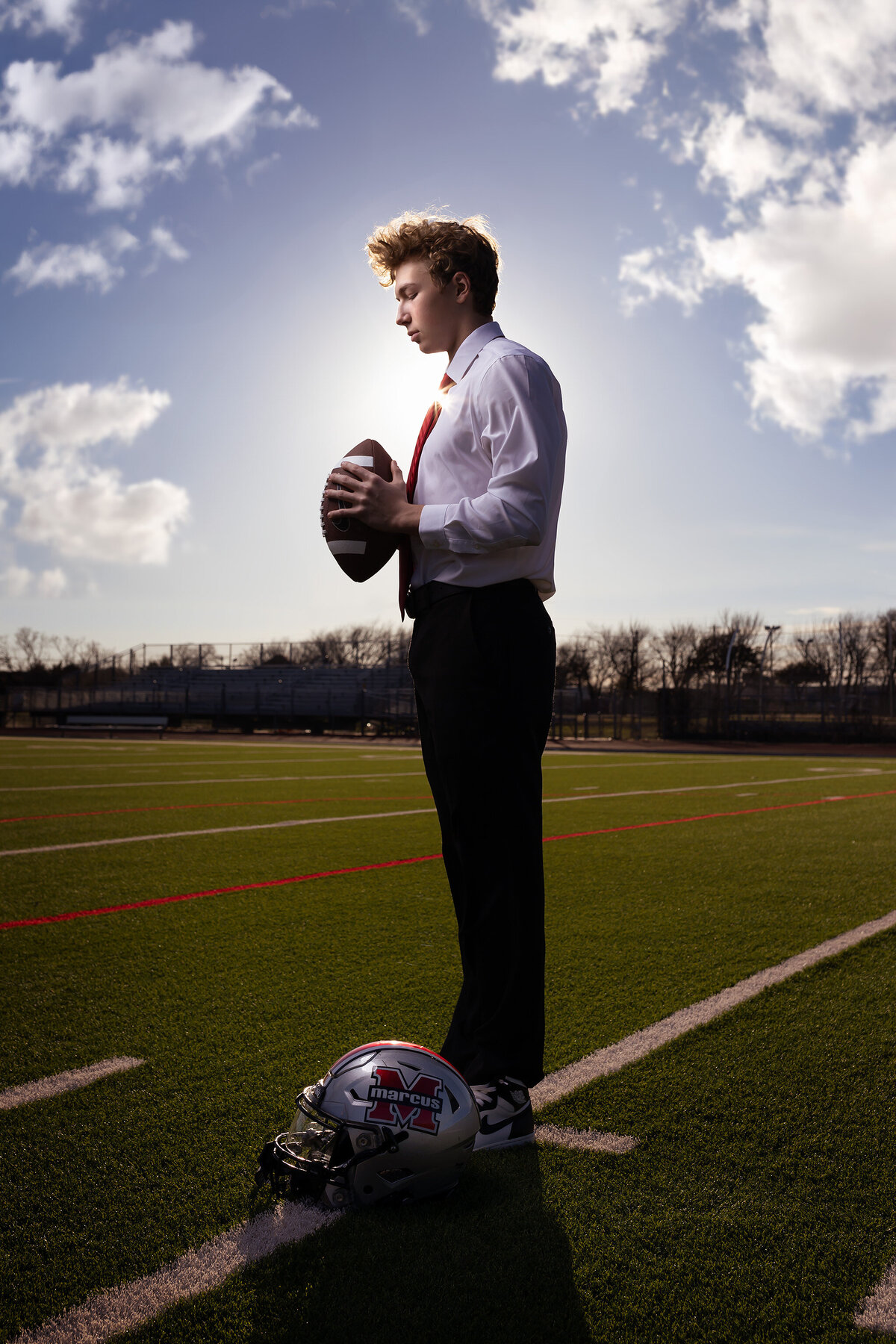 A high school senior in a suit holds a football on the field, captured by senior photography Dallas TX.