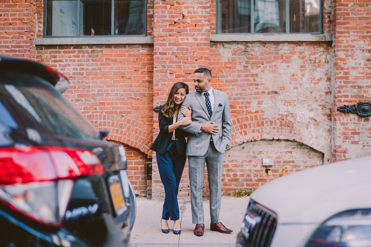 A couple standing on washington street near the brooklyn bridge in dumbo in front of a brick buiilding