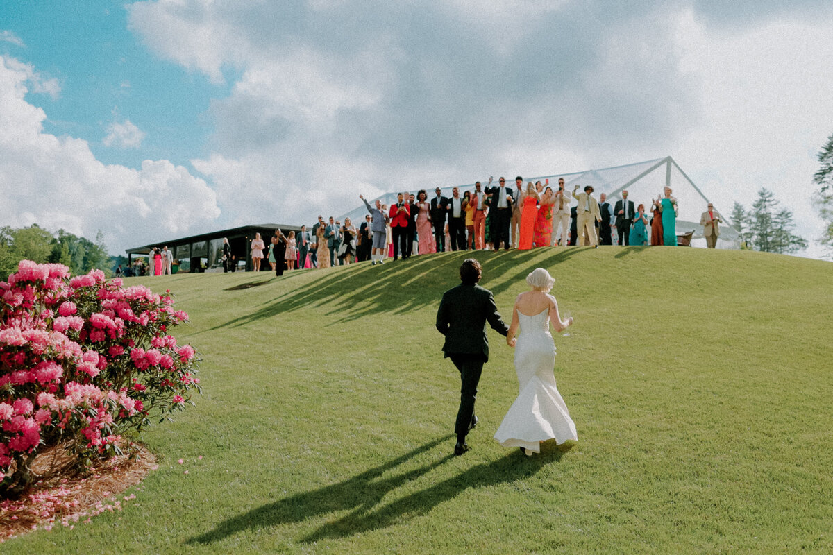 Bride and Groom run up a hill towards their friends at their wedding
