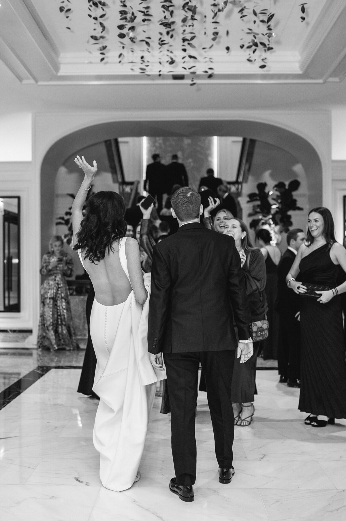 A black and white photo of a couple walking through their elegant wedidng venue surrounded by guests