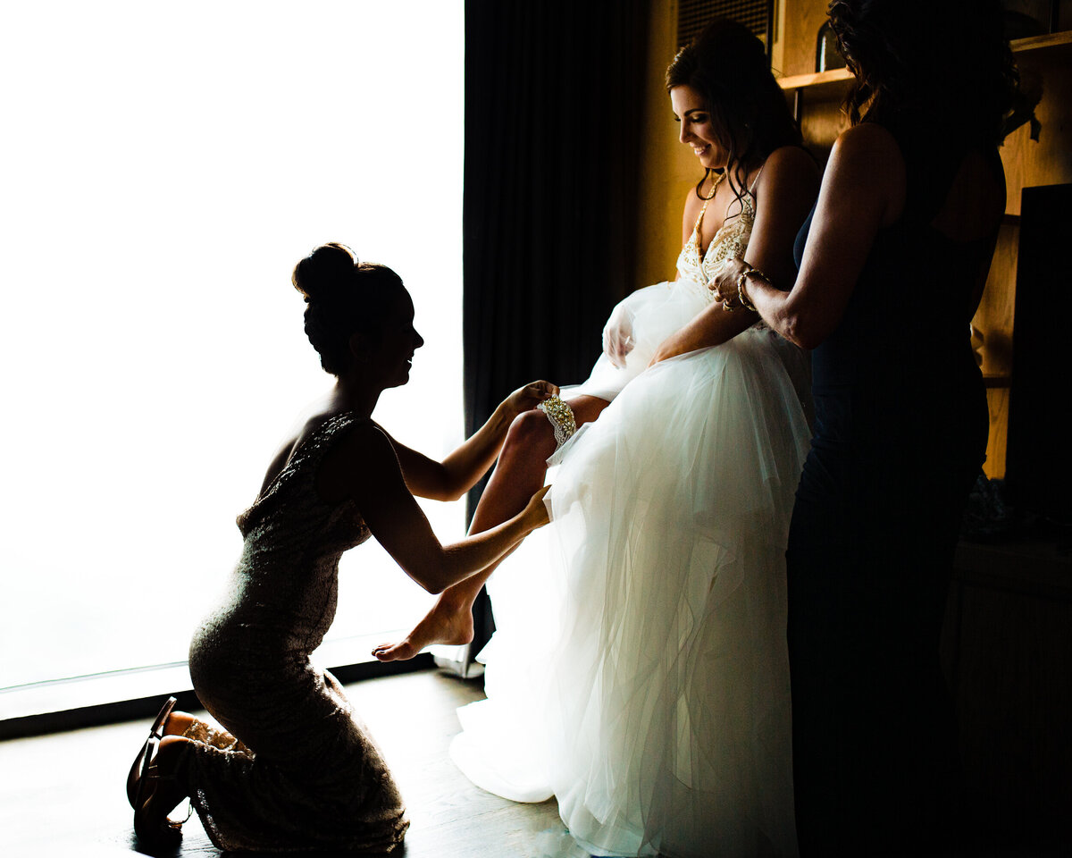 One of the top wedding photos of 2020. Taken by Adore Wedding Photography- Toledo, Ohio Wedding Photographers. This photo is of a brides sister helping the bride put on her garter after the bride got dressed at the Renaissance Hotel in Toledo Ohio