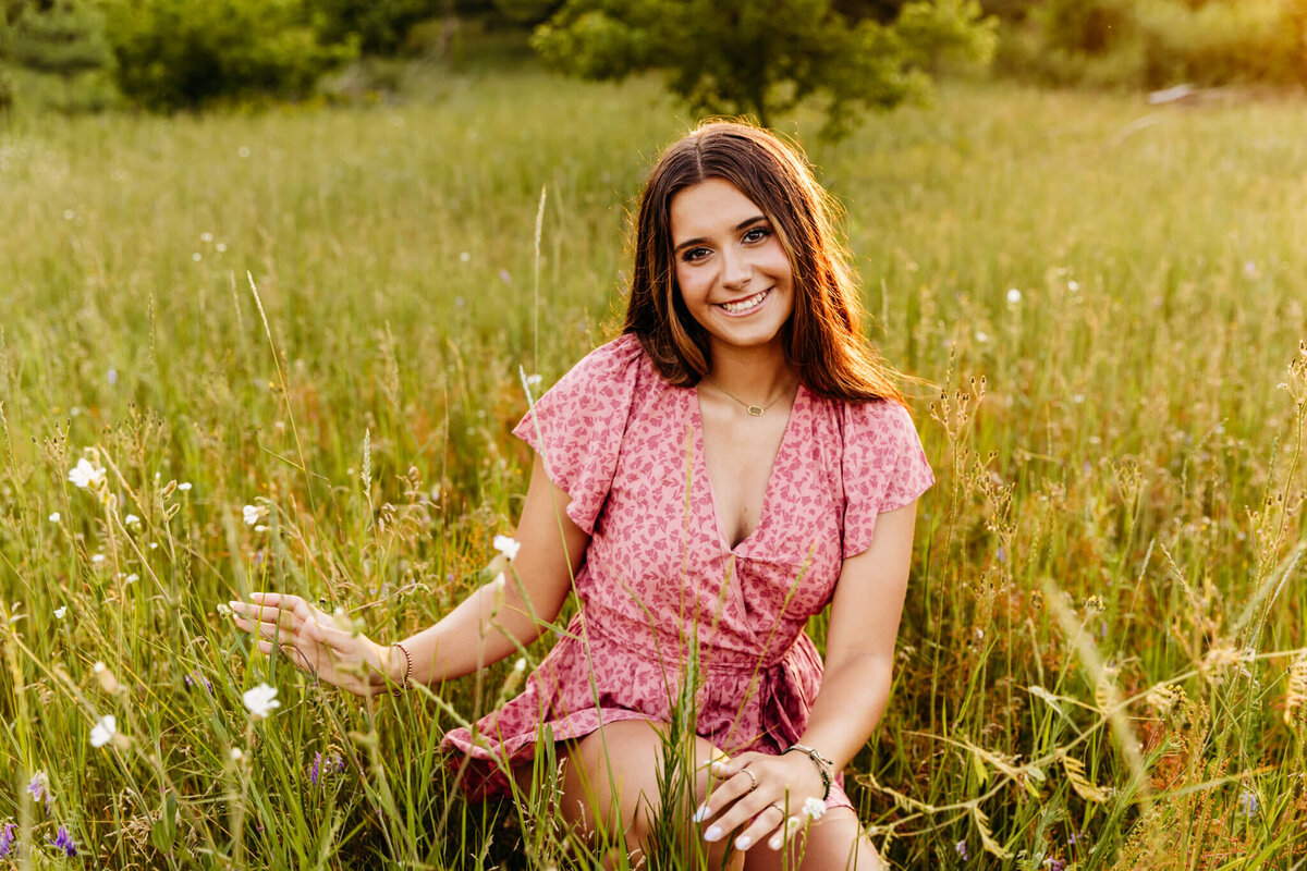 pretty teenage girl in a pink outfit playing with the wildflowers as she kneels in a field near Green Bay