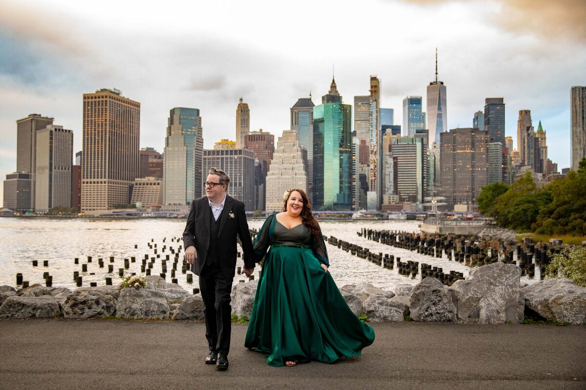 A couple holding hands and walking with a city skyline behind them.