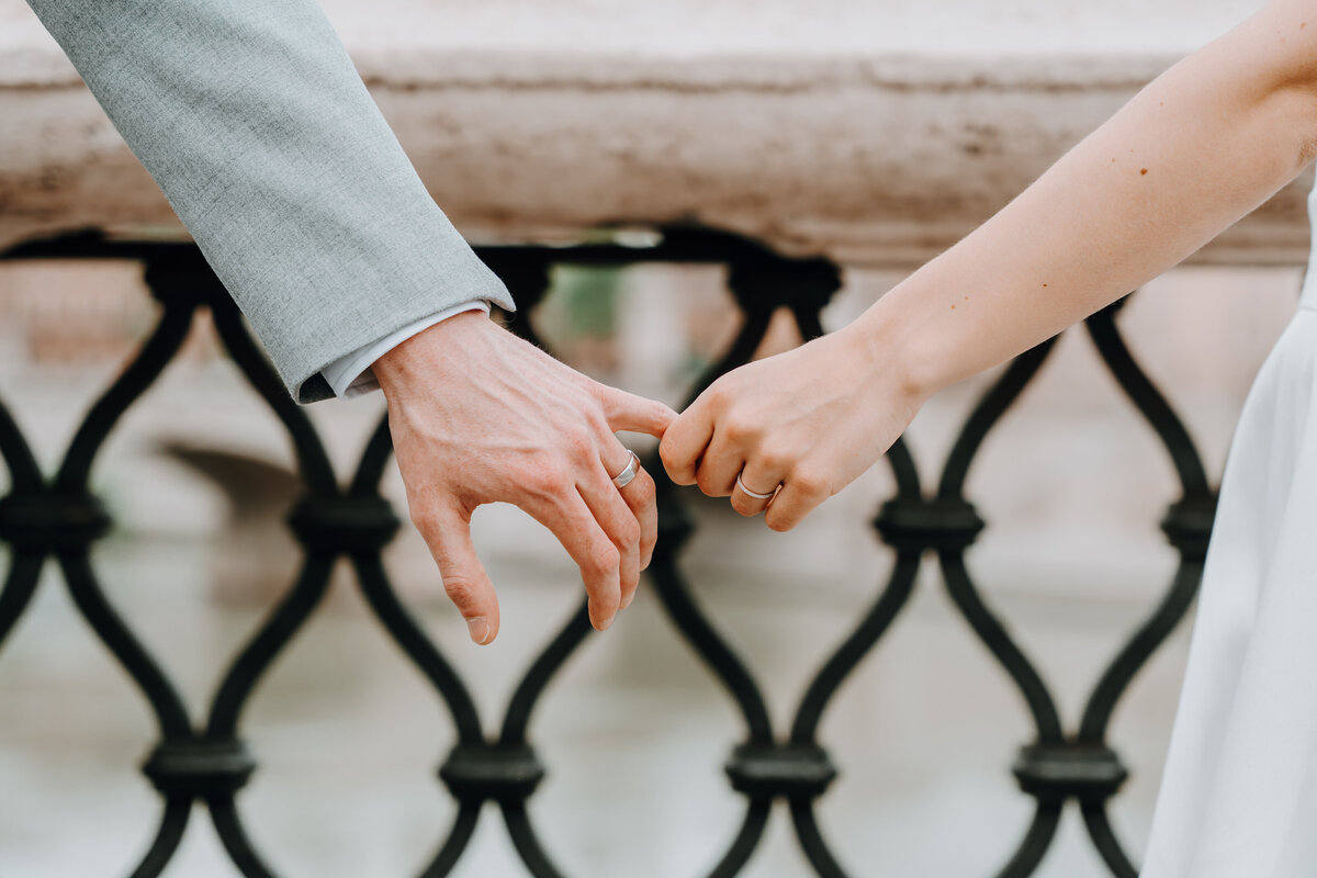 Couple holding hands through metal railing with Rome skyline behind.