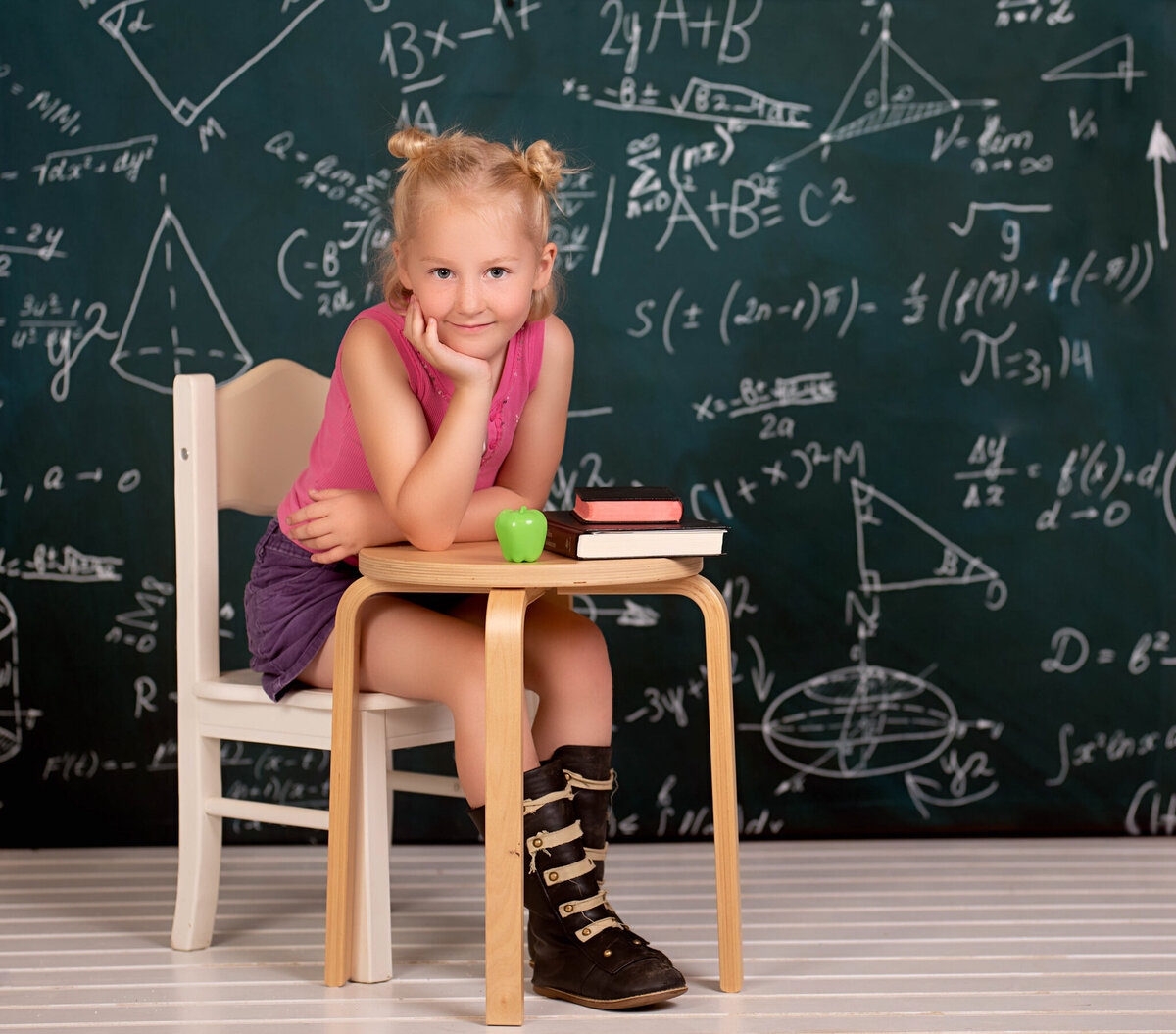 Charming portrait of a young girl sitting at a school desk with a chalkboard backdrop, captured in Overland Park, Kansas. Ideal for families seeking creative and milestone child photography in the Kansas City area.