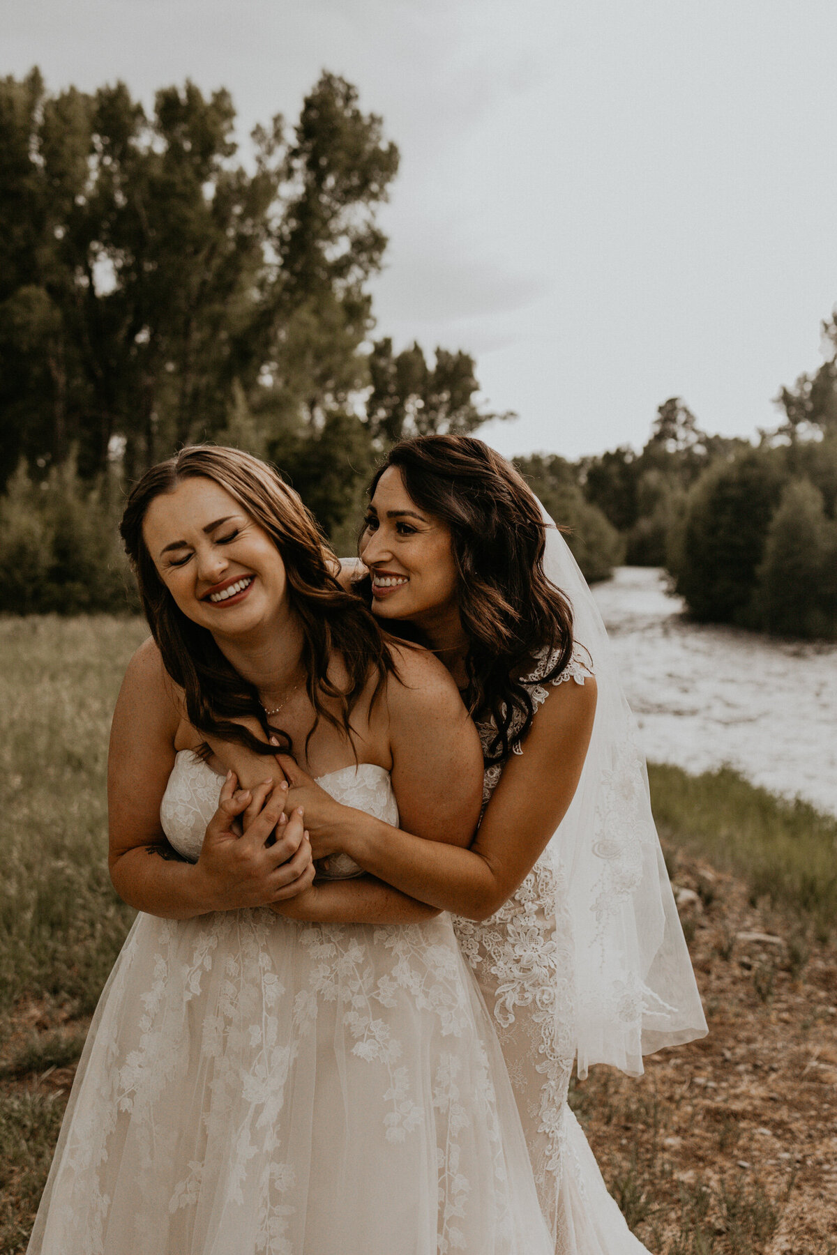 same sex couple holding each other and smiling in front of a river