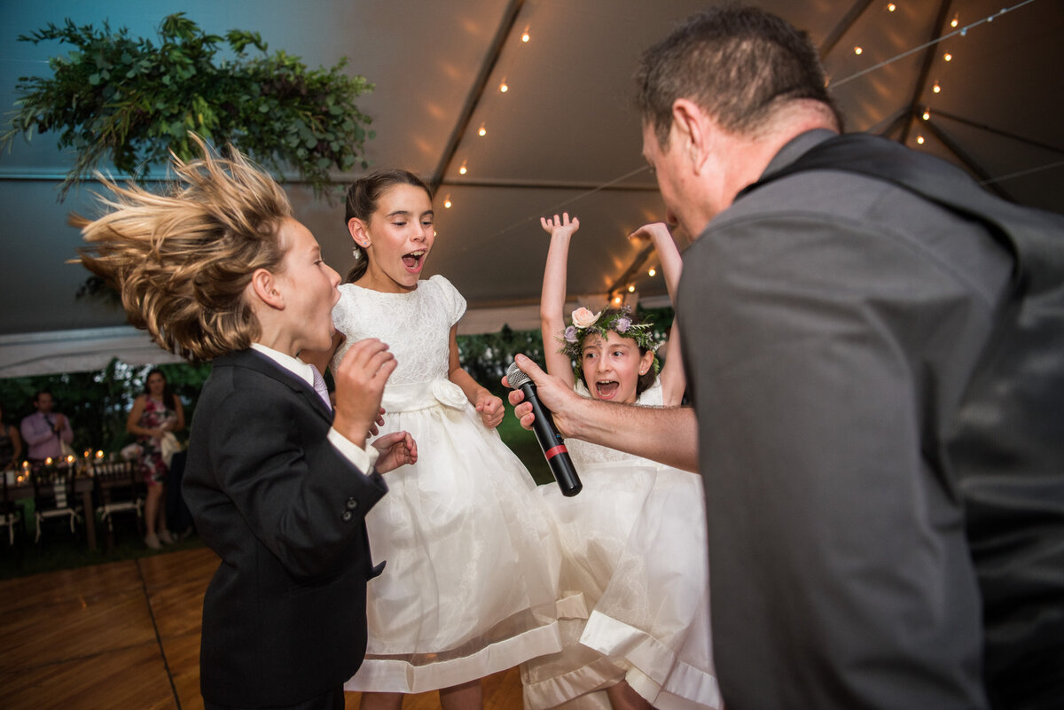 Kids singing and dancing at a wedding reception as someone holds a mic out to them 