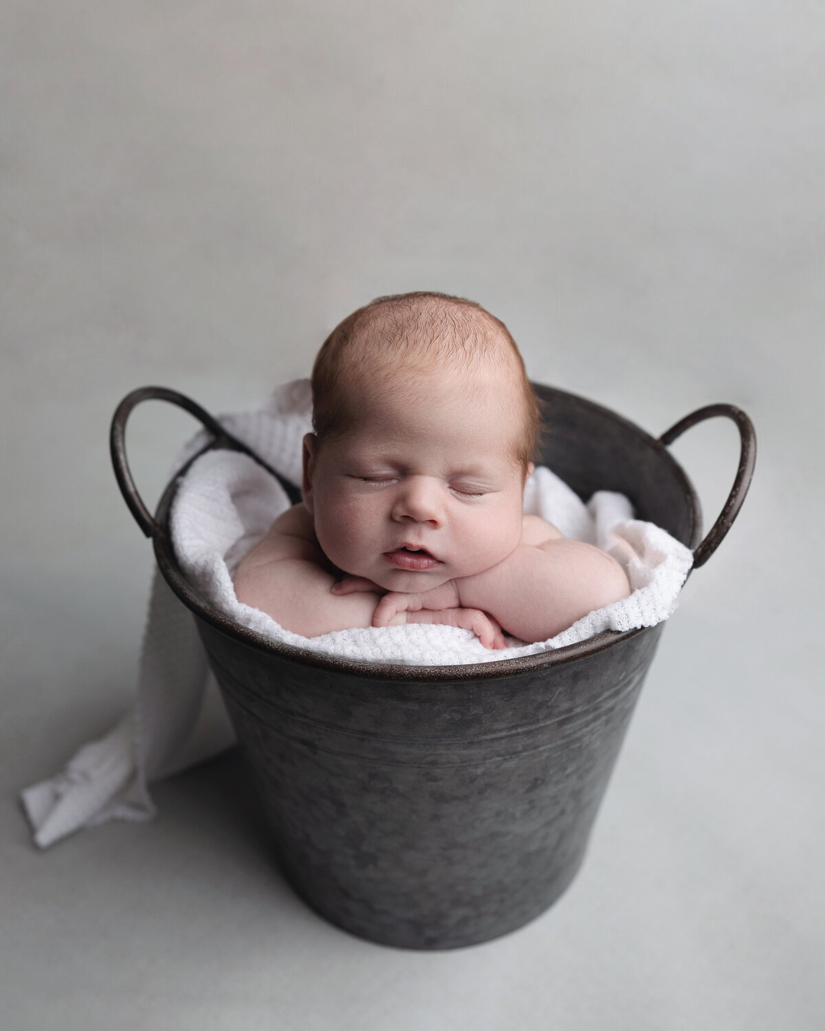 Baby sleeps in bucket with hands under his chin .