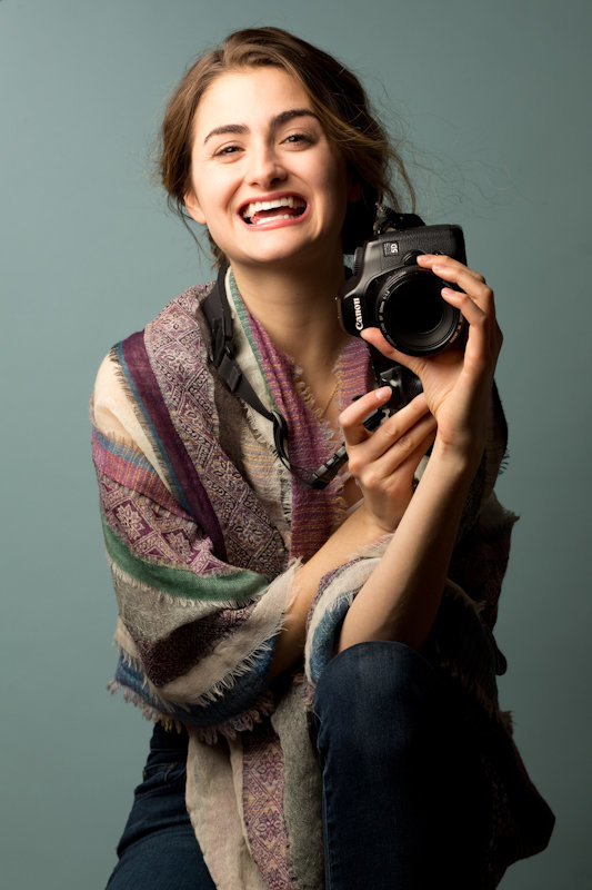 Laura Volpacchio holds her camera and smiles big for a studio photo