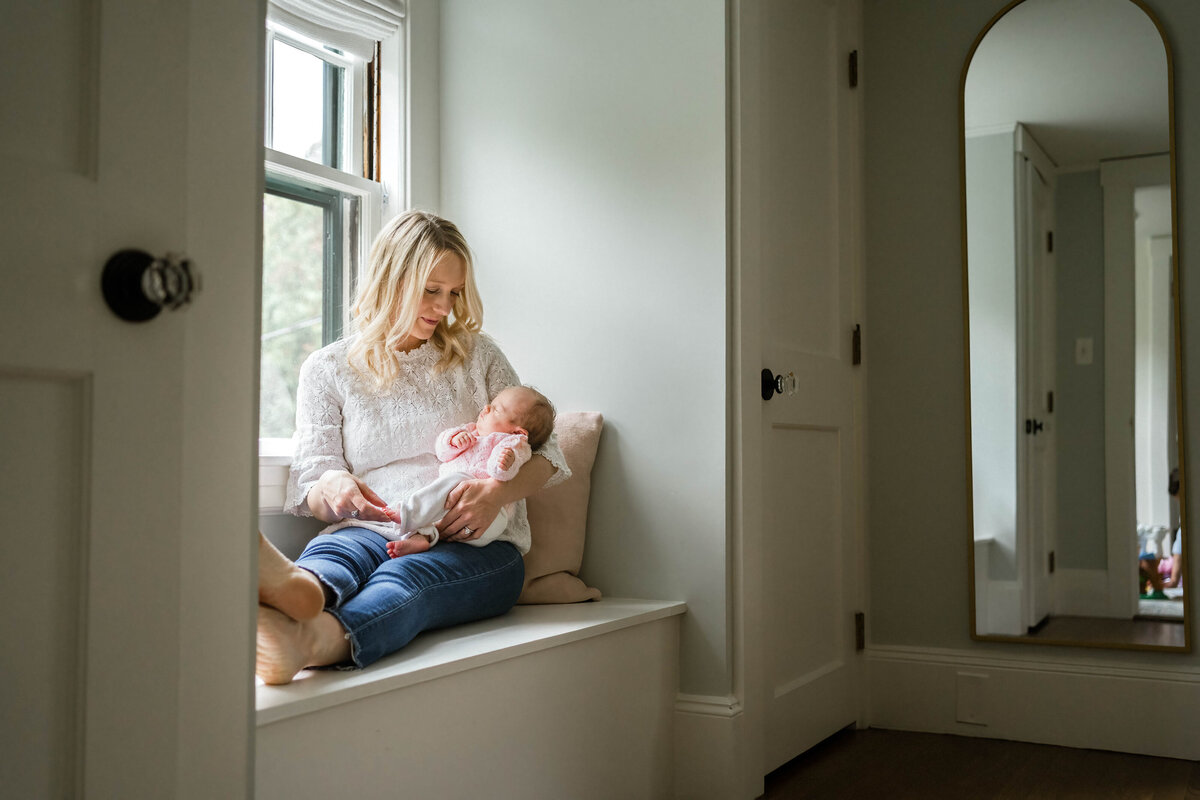 Mom sitting in window seat looking at baby girl in Wayland