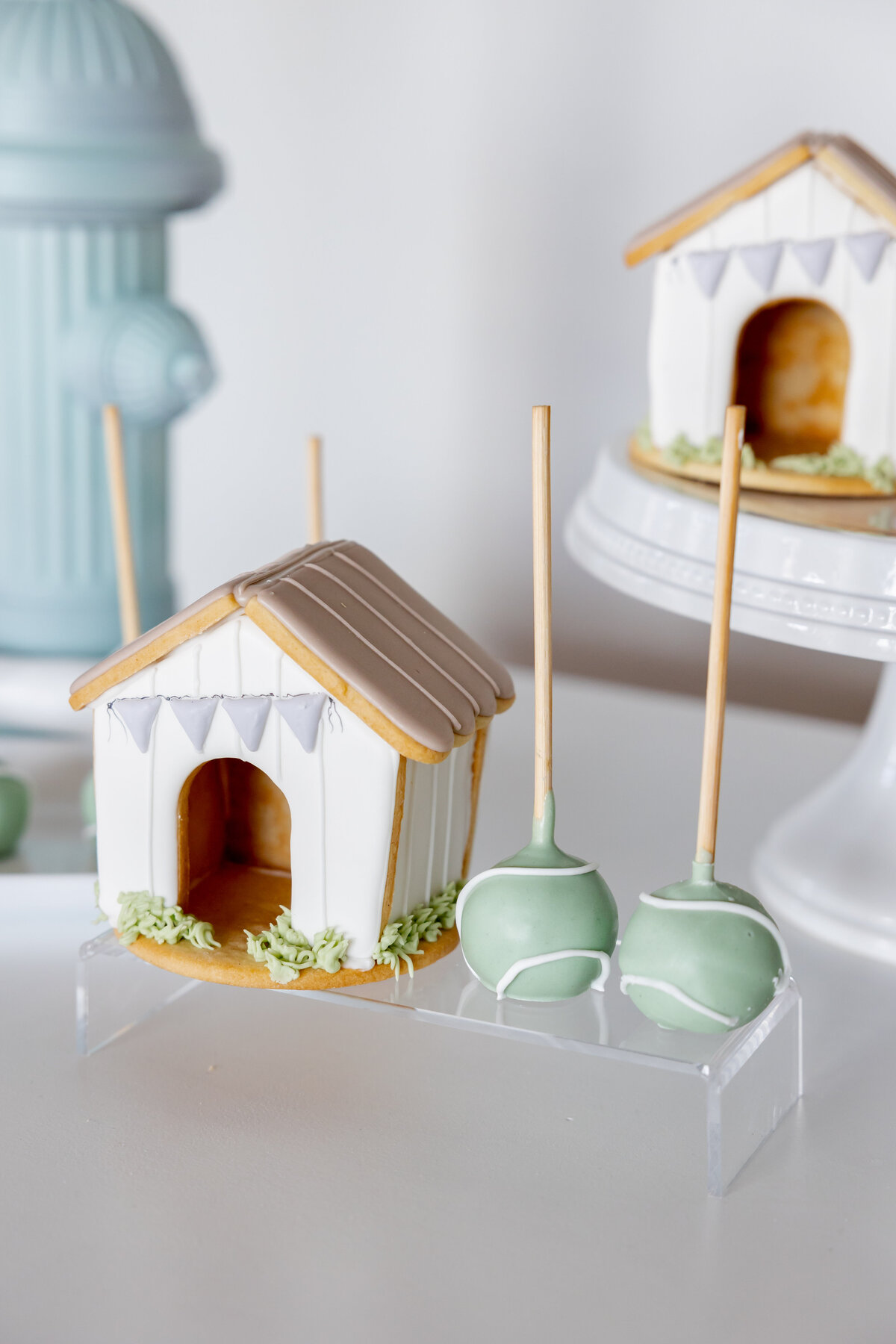 Dog house cookie and tennis ball cake balls on acrylic risers. 