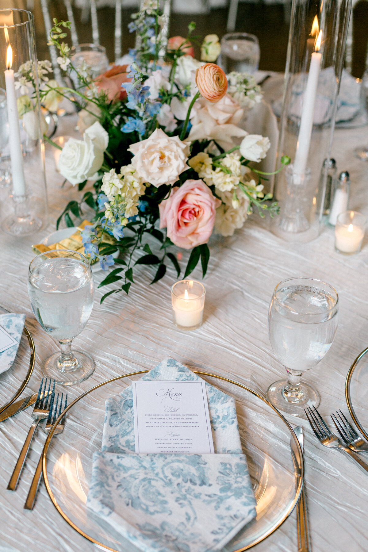 Wedding reception table setting with blue floral napkins and colorful floral arrangements