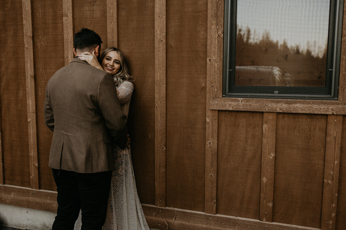 newlyweds standing against a cabin in their wedding attire