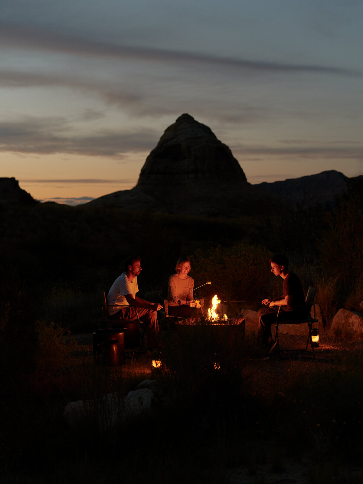 A group of travelers gathered around a glowing campfire at Amangiri, surrounded by the serene desert landscape at dusk. 