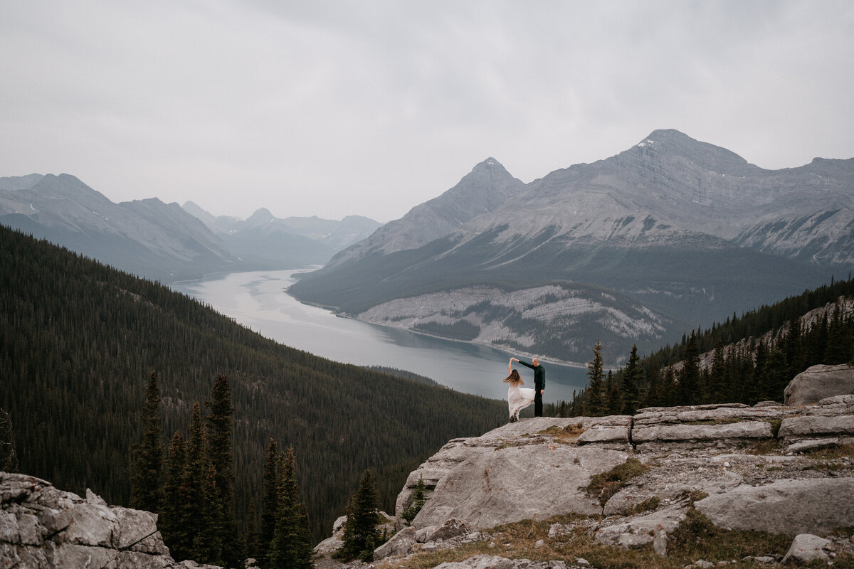 Groom twirls bride overlooking Spray Lakes from West Wind Pass