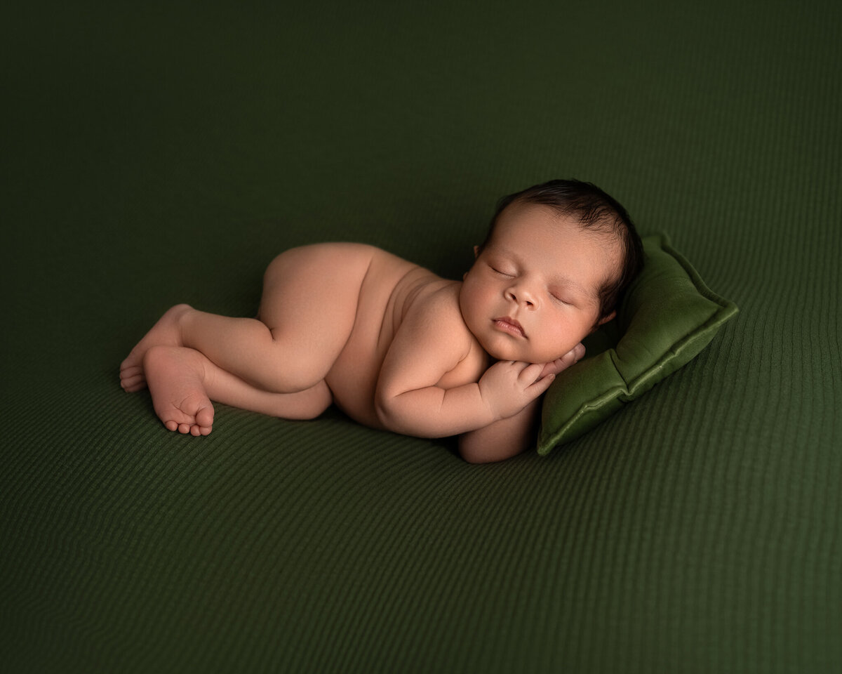 Newborn baby boy sleeping nude on green fabric with matching mini pillow | Austin newborn photographer near Leander and Westlake